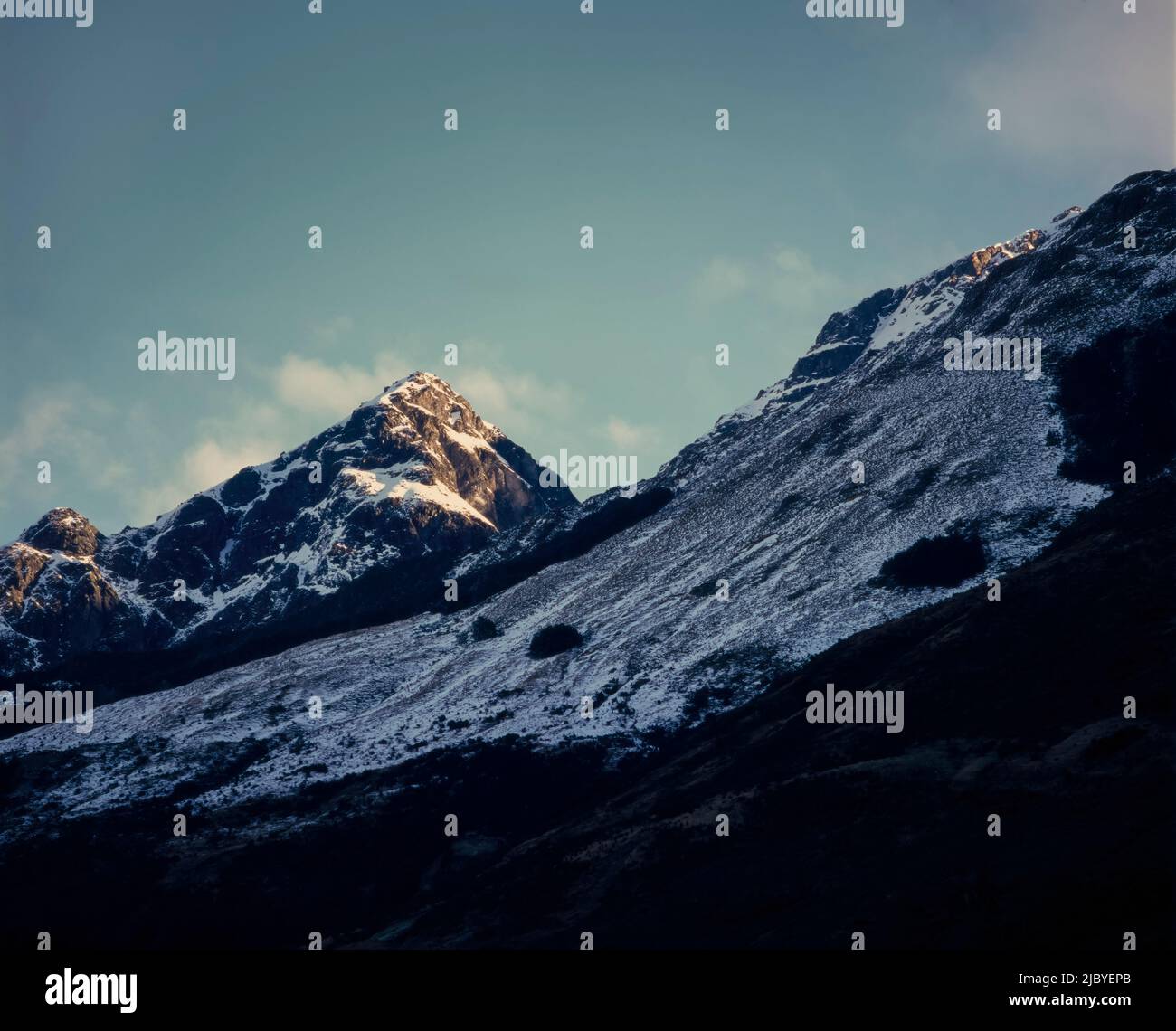 Primer plano de la luz del sol de la mañana golpeando la cima de las montañas con una ligera capa de nieve contra el cielo azul Foto de stock