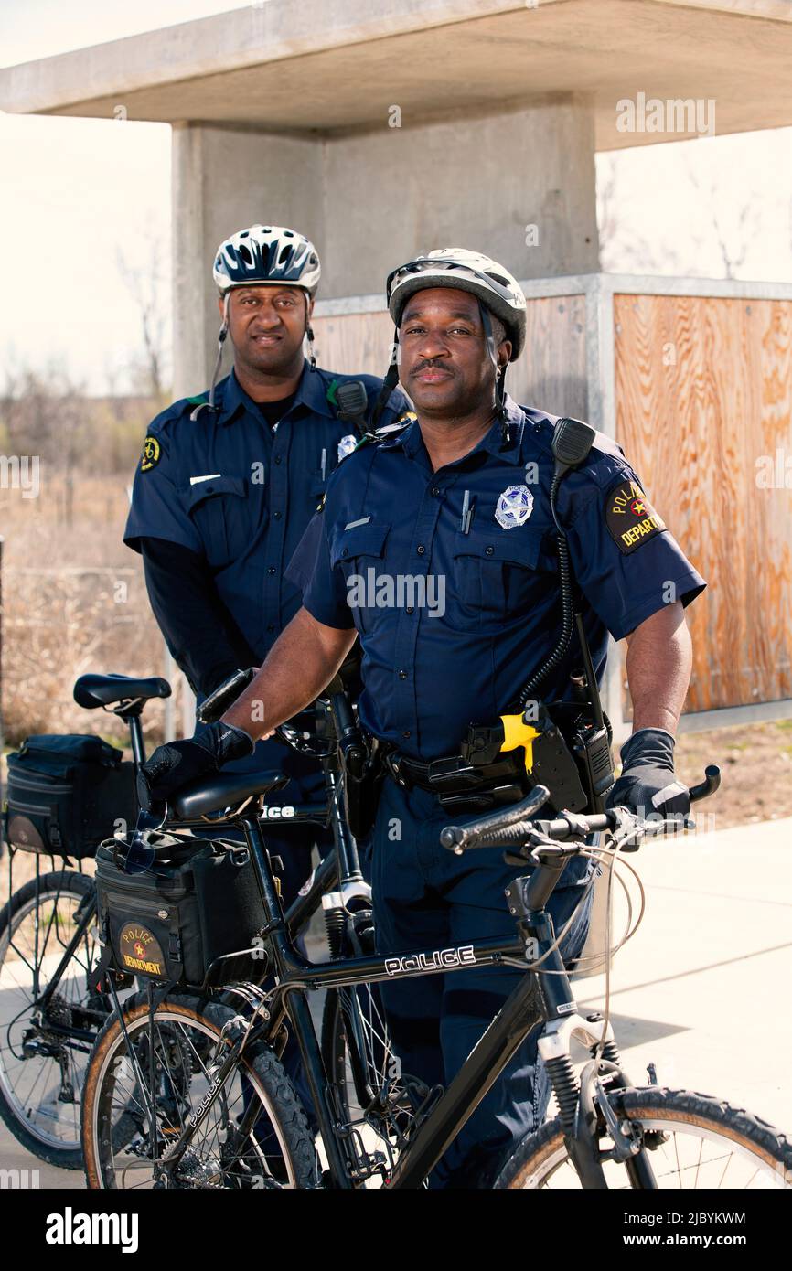 Retrato de los oficiales de policía de bicicleta de pie afuera con sus bicicletas mirando hacia la cámara sonriendo Foto de stock