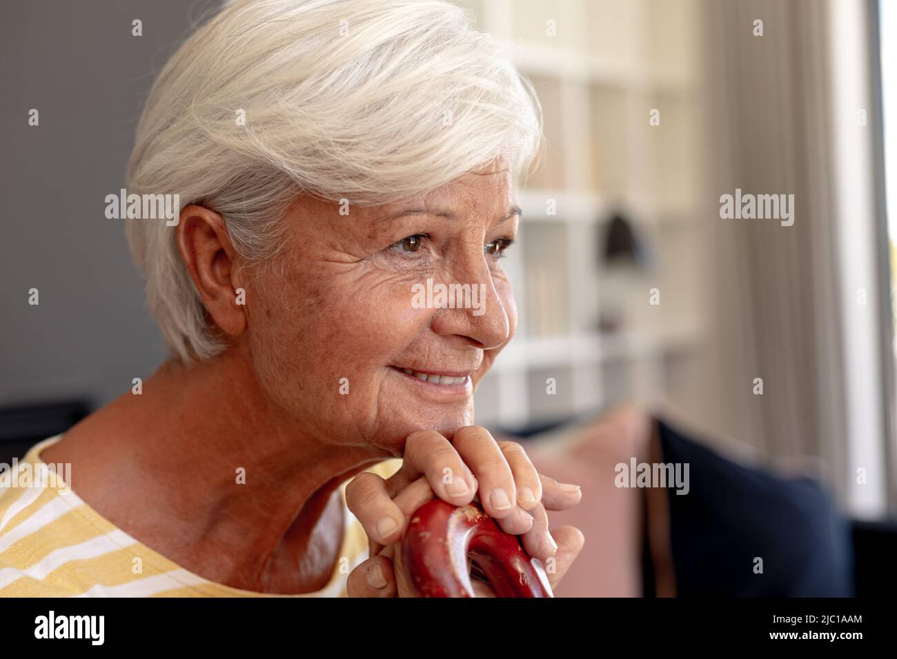 Primer plano de la mujer caucásica de edad avanzada con el pelo gris sosteniendo bastón mientras contemplaba en casa Foto de stock