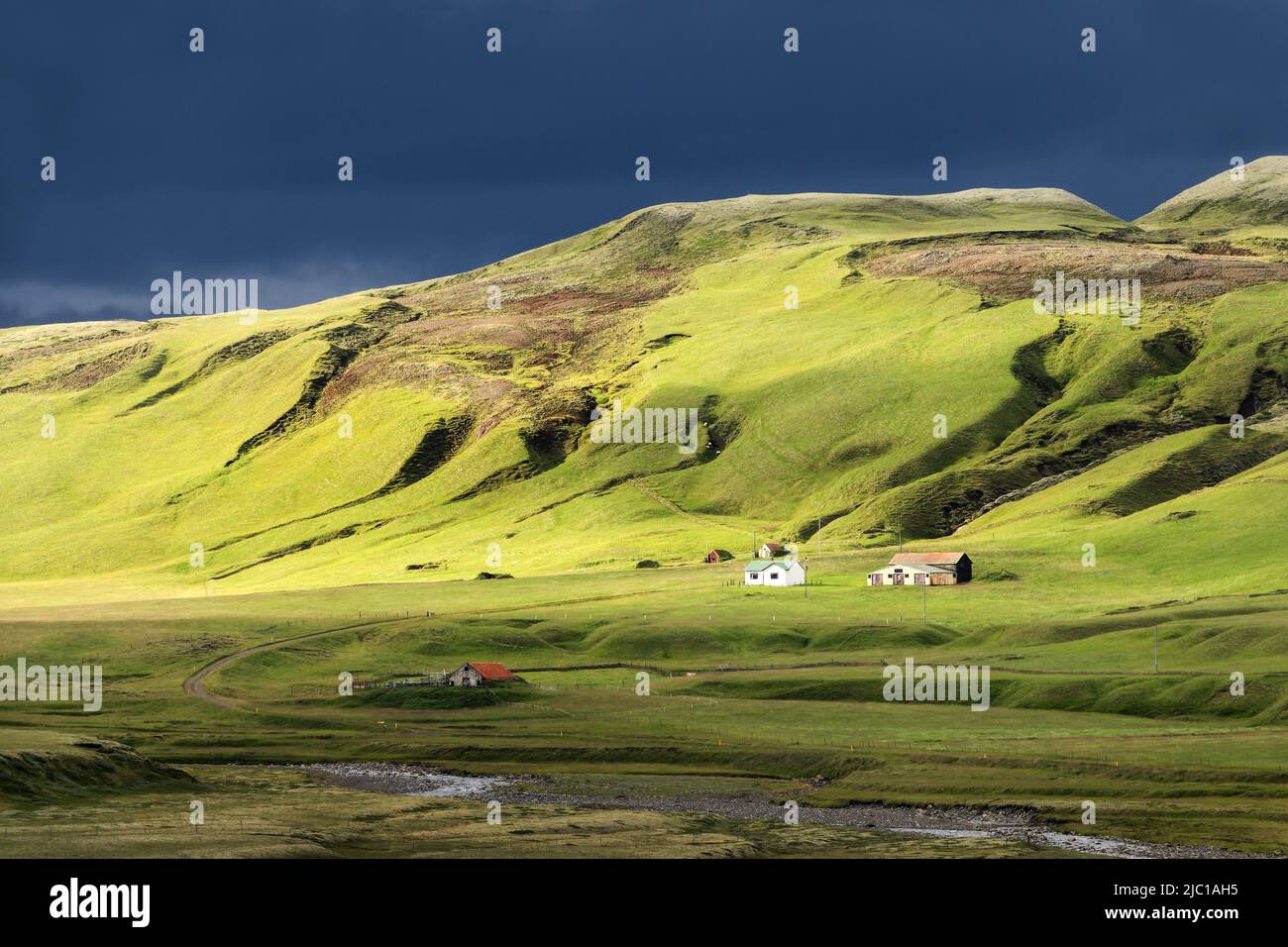Sol con nubes oscuras sobre una granja en la montaña, paisaje escénico en Islandia Foto de stock