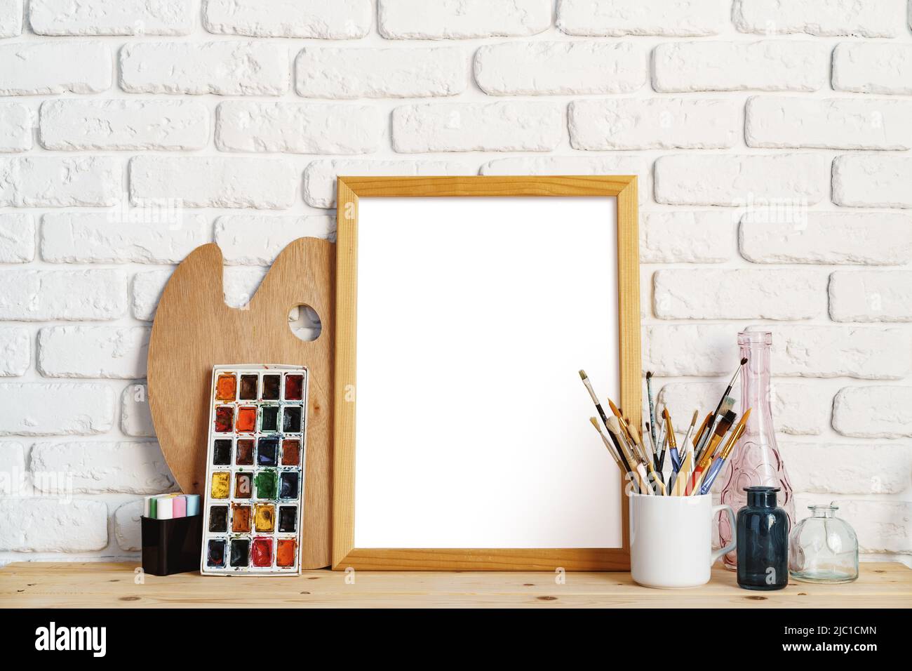 Marco de fotos como caballete con las herramientas del artista en la mesa  de madera contra la pared de ladrillo blanco Fotografía de stock - Alamy