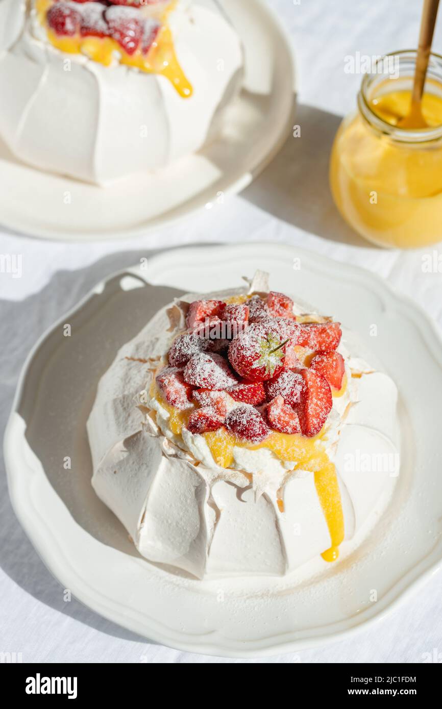 Postres clásicos de Pavlova con fresa, nata montada y limón y tarro con limón rizado en luces solares. Foto de stock