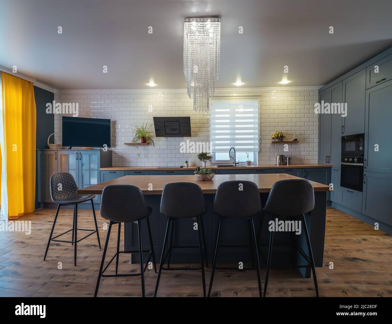 Interior de cocina moderna en azul con detalles amarillos y suelo de madera con una gran mesa en el medio de la habitación, zona de cocina y sofá para relajarse Fotografía de Interior de cocina moderna en azul con detalles amarillos y suelo de madera con una gran mesa en el medio de la habitación, zona de cocina y sofá para relajarse Fotografía de