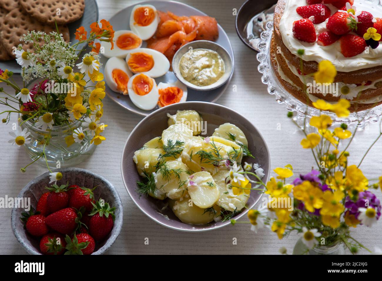 Comida escandinava de mediados de verano con pastel de fresa y crema, ensalada de patata, salmón y huevos Foto de stock