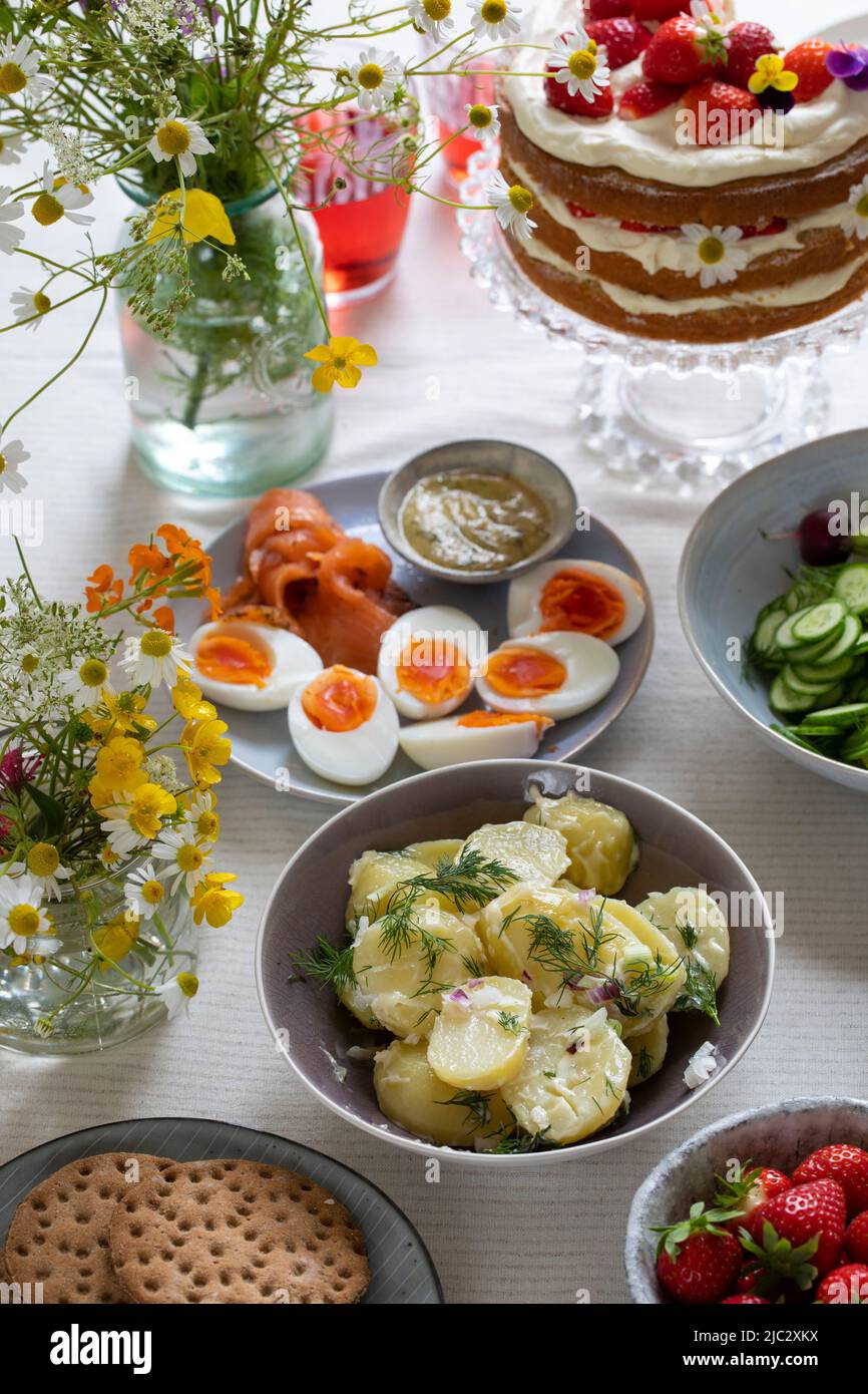 Comida escandinava de mediados de verano con pastel de fresa y crema, ensalada de patata, salmón y huevos Foto de stock
