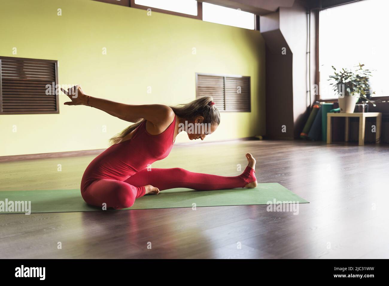 Una practicante de yoga realiza una variante del ejercicio Prasarita padottanasana, doblándose hacia delante con los brazos extendidos detrás de su espalda, sentada Foto de stock