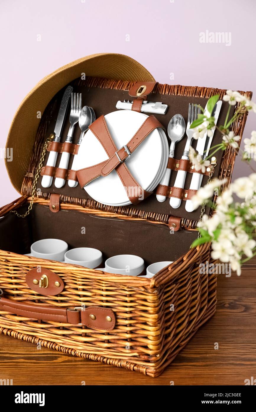 Cesta de mimbre con vajilla para picnic en la mesa cerca de la