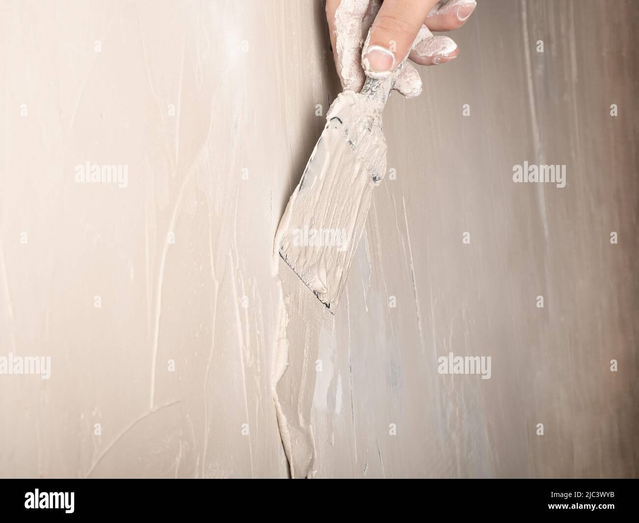 El maestro está aplicando masilla blanca en una pared y manchando con una  espátula en una sala de renovación de la casa durante el día