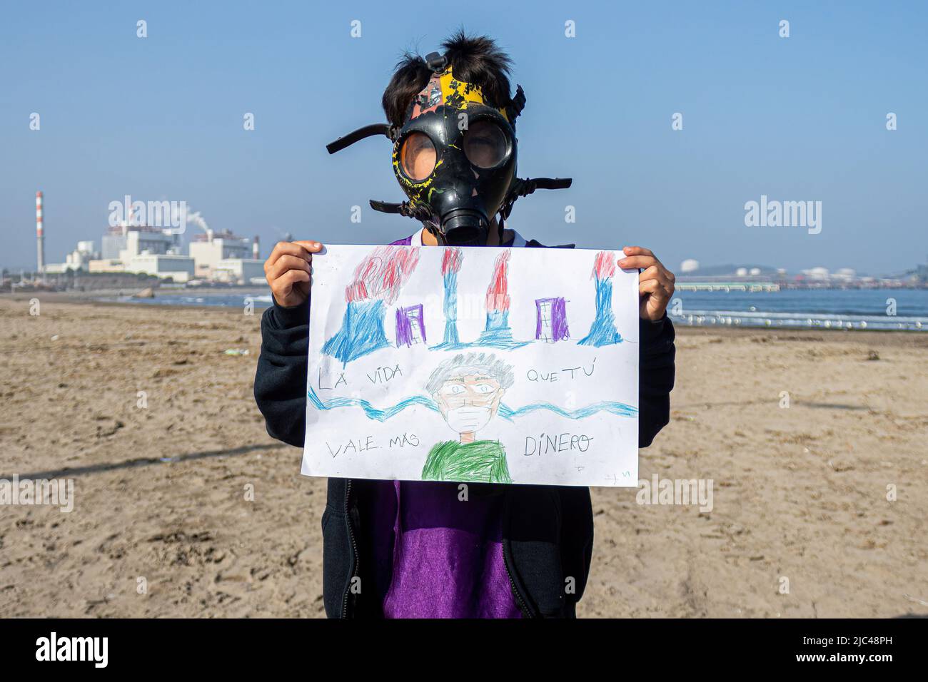 Un niño que lleva una máscara de gas sostiene un cartel en la playa  Puchuncavi, cerca de la planta termoeléctrica AES Gener, en la región de  Valparaíso, durante una protesta para exigir