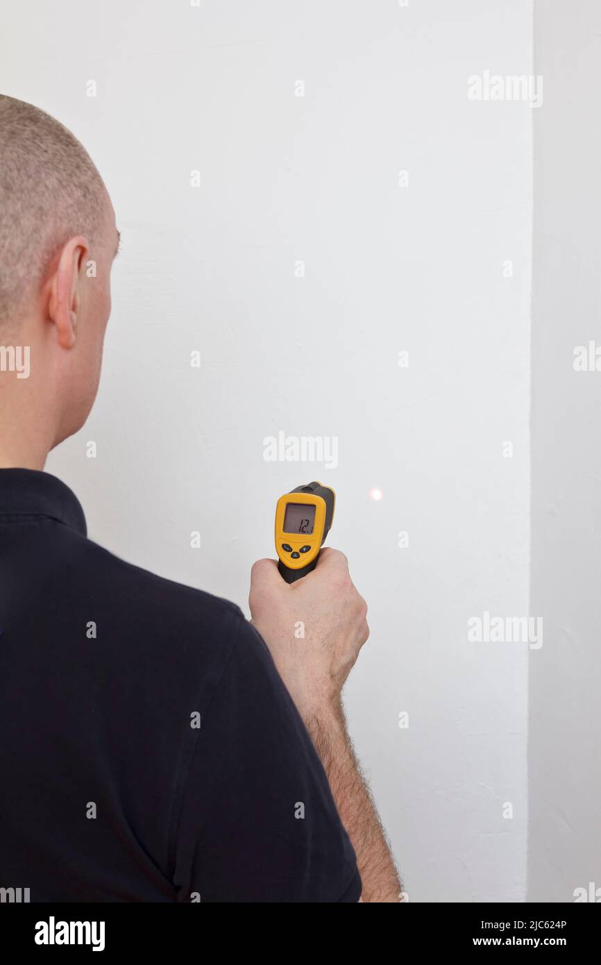 Concepto de ahorro de energía: Hombre que mide la temperatura de una pared blanca externa con un termómetro de infrarrojos o láser. Foto de stock