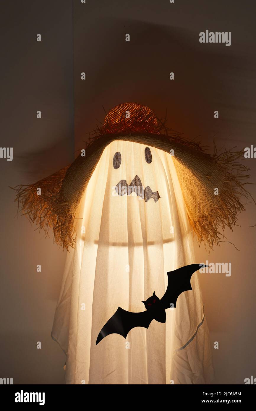 Lámpara iluminada cubierta con sábana colocada en habitación oscura, sábana  blanca con cara fea dibujada y sombrero de paja Fotografía de stock - Alamy