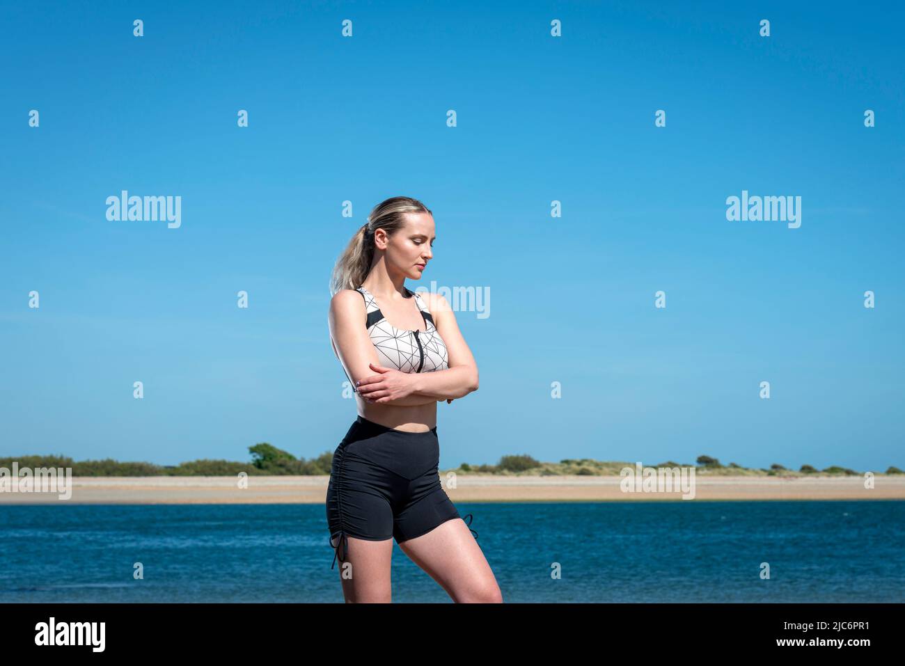 mujer deportiva de pie junto a la costa con pantalones cortos con los brazos cruzados. Foto de stock