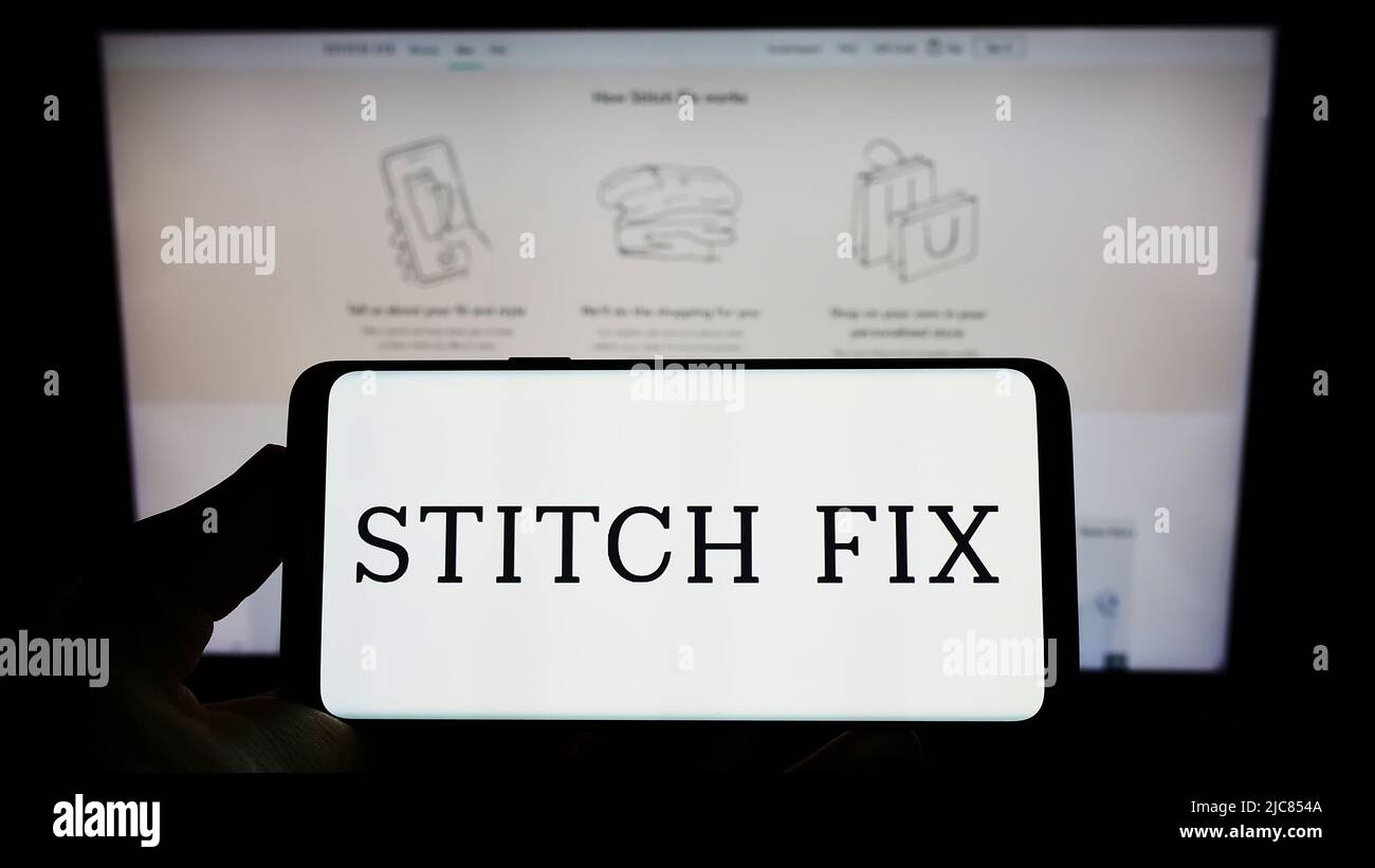 Persona que sostiene el teléfono móvil con el logotipo de la compañía de estilo estadounidense Stitch Fix Inc. En la pantalla frente a la página web del negocio. Enfoque en la pantalla del teléfono. Foto de stock
