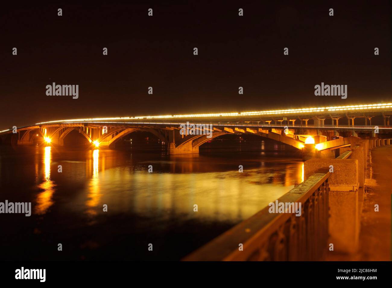 Las luces de la calle en el puente se reflejan en el río por la noche Foto de stock