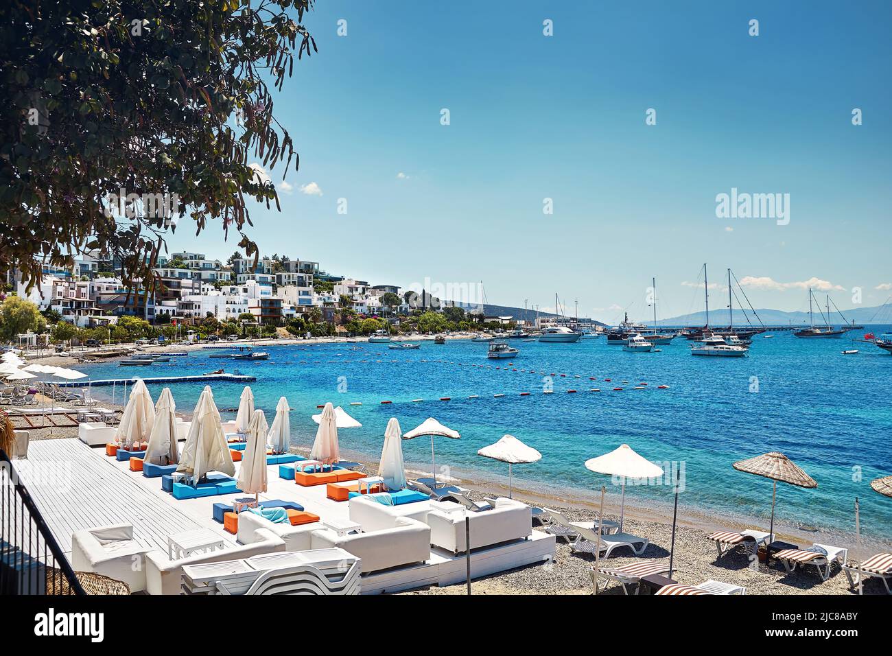 Vista de la playa Bodrum con sombrilla y hamacas cerca del mar Egeo cerca de hotel privado y barcos de vela, yates en Bodrum ciudad de Turquía. Foto de stock