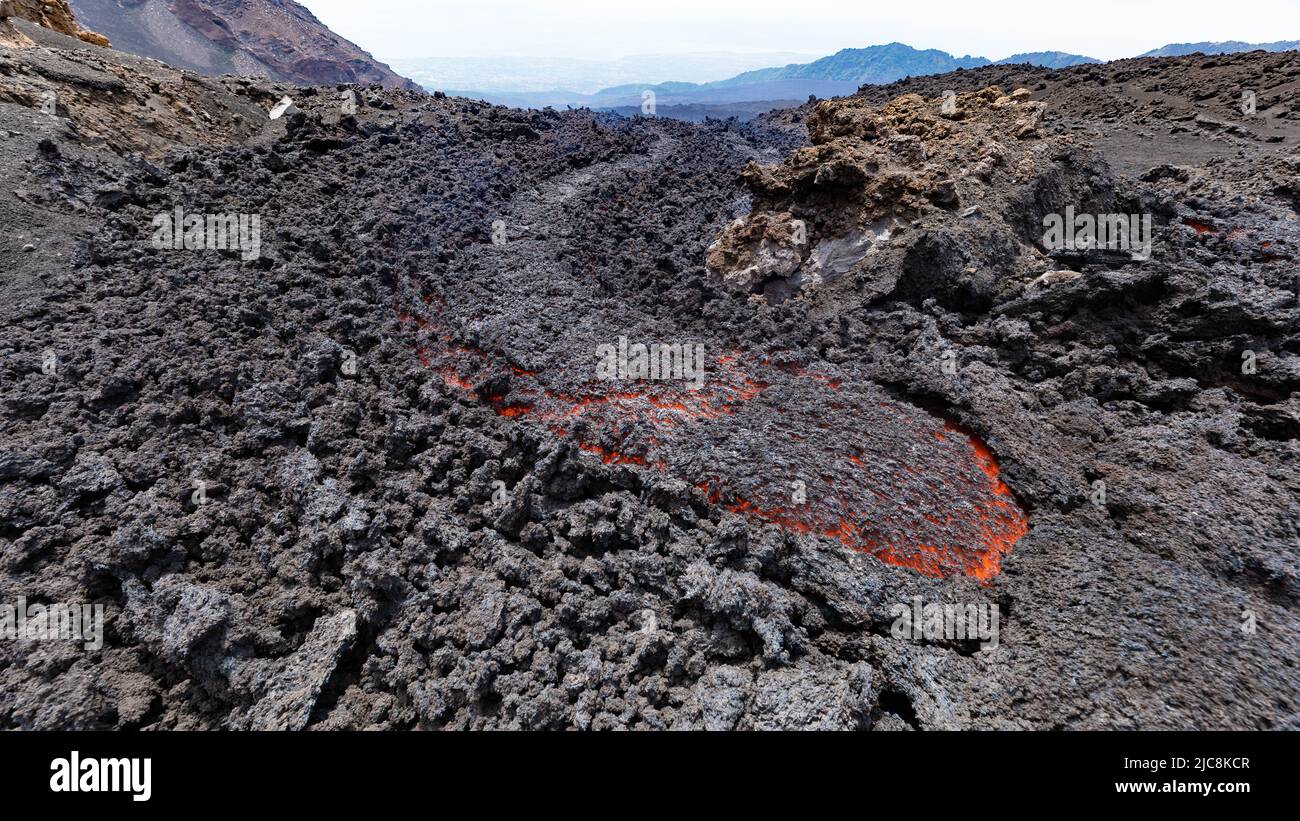 Lava incandescente fluye en el volcán Etna en Sicilia en el Valle del Bove con humo y lava canal de flujo Foto de stock