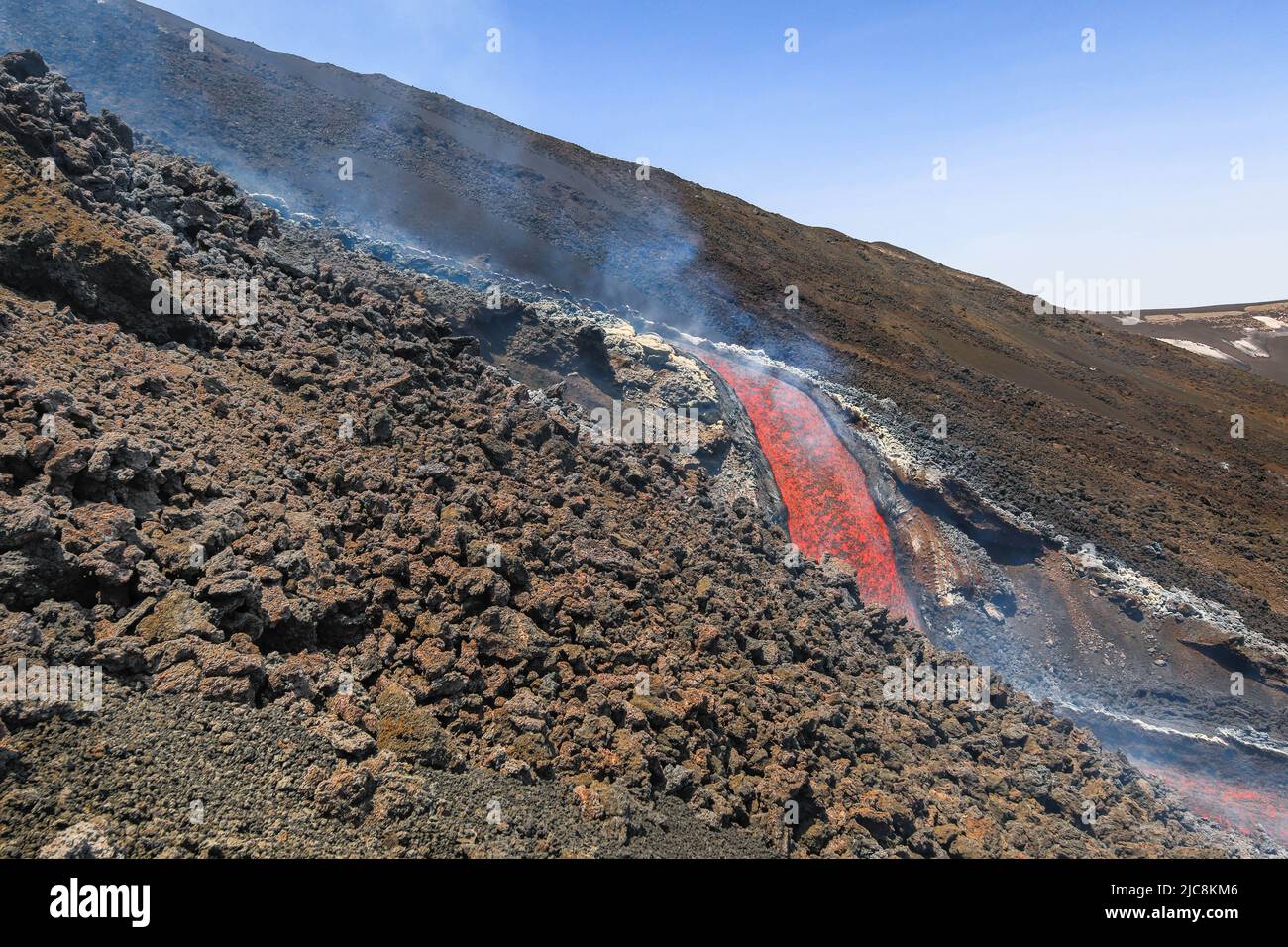La caída de lava del Etna que fluye sobre el volcán de Sicilia en el Valle del Bove con el humo y el canal de flujo de lava Foto de stock