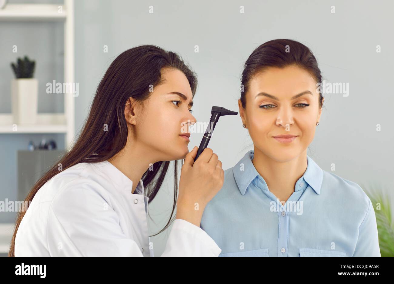 El médico de ENT utiliza un otoscopio para examinar el oído de la mujer joven durante el chequeo médico en el consultorio Foto de stock