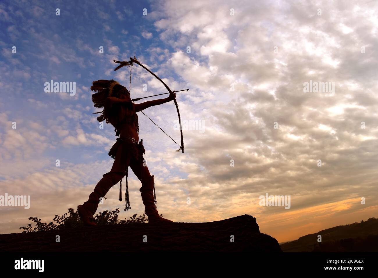 Una joven india americana nativa se perfila frente al cielo de la noche. Se enorgullece de sus armas a su lado. Foto de stock