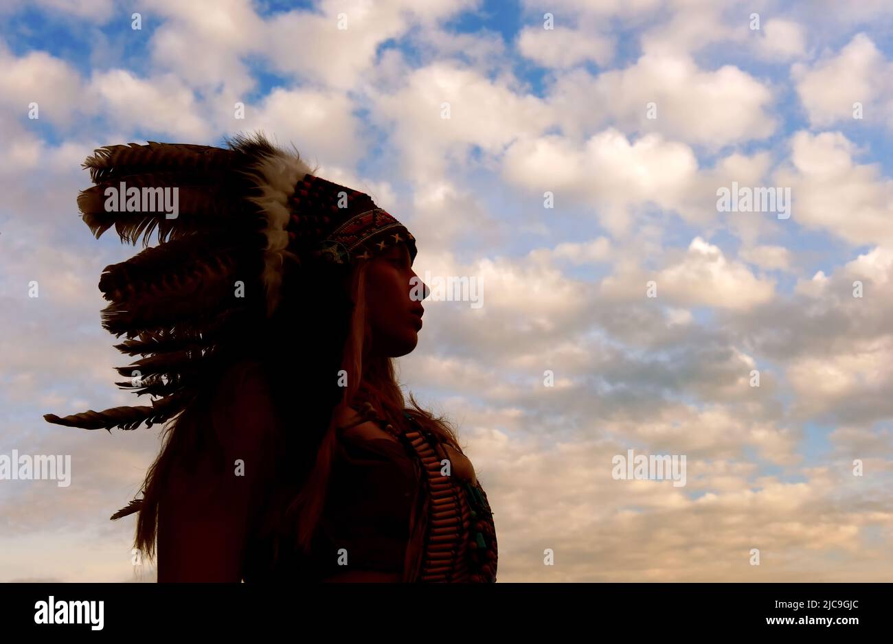 Una joven india americana nativa se perfila frente al cielo de la noche. Se enorgullece de sus armas a su lado. Foto de stock