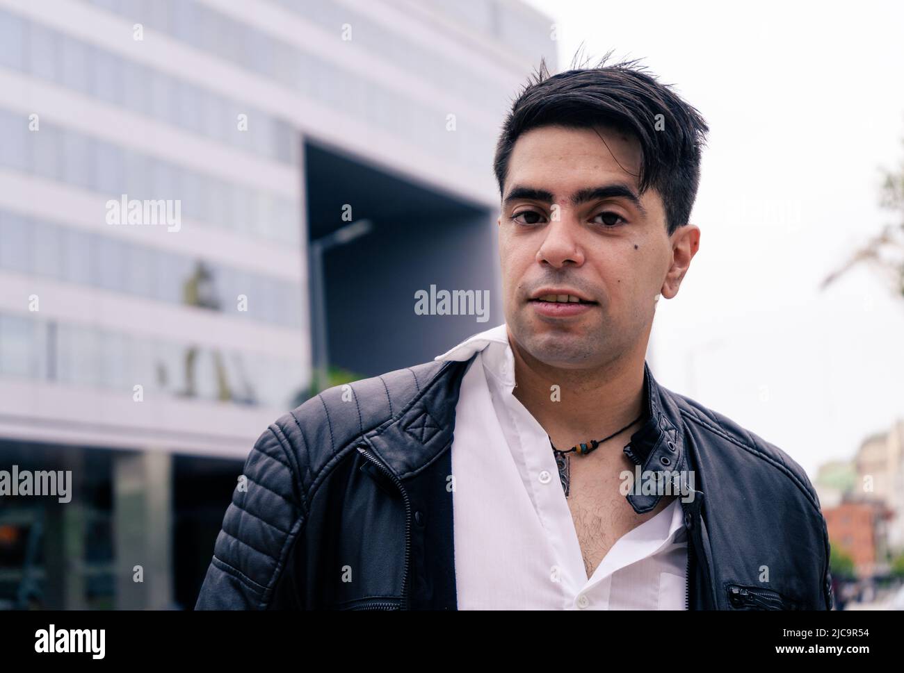 Atractivo hombre latino en una chaqueta negra y camisa blanca con un  moderno edificio detrás Fotografía de stock - Alamy
