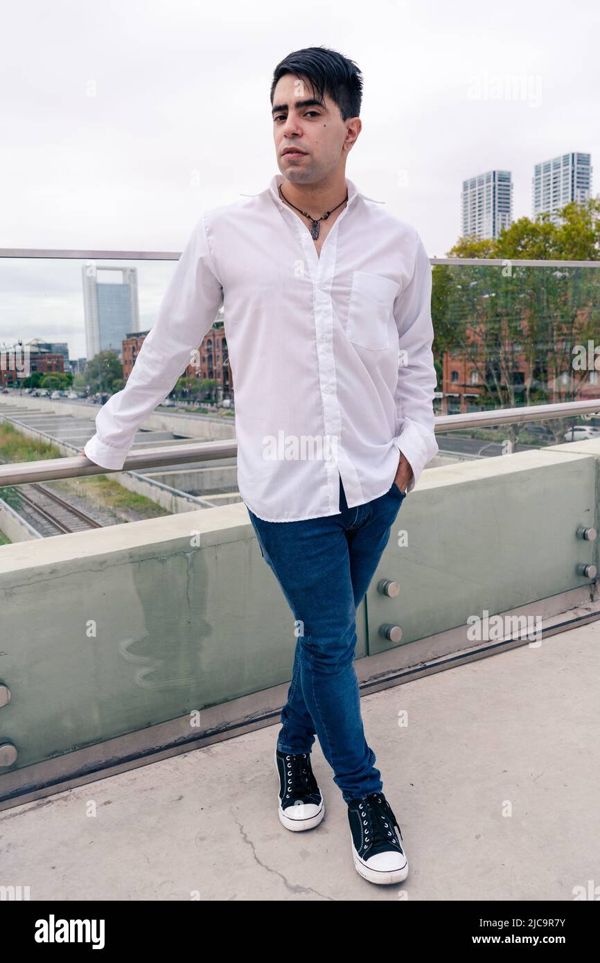 Atractivo joven latino con pantalones oscuros y una camisa blanca en una escena urbana. Atractivo joven latino con pantalones oscuros y una camisa blanca en una zona urbana Foto de stock