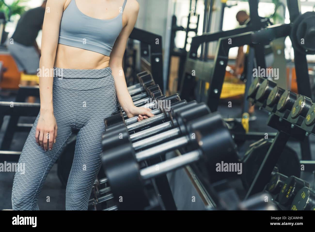 Mujer blanca delgada irreconocible con sujetador deportivo y leggings estampados que alcanzan una gran mancuerna. Disparo en interiores. Fotografías de alta calidad Foto de stock