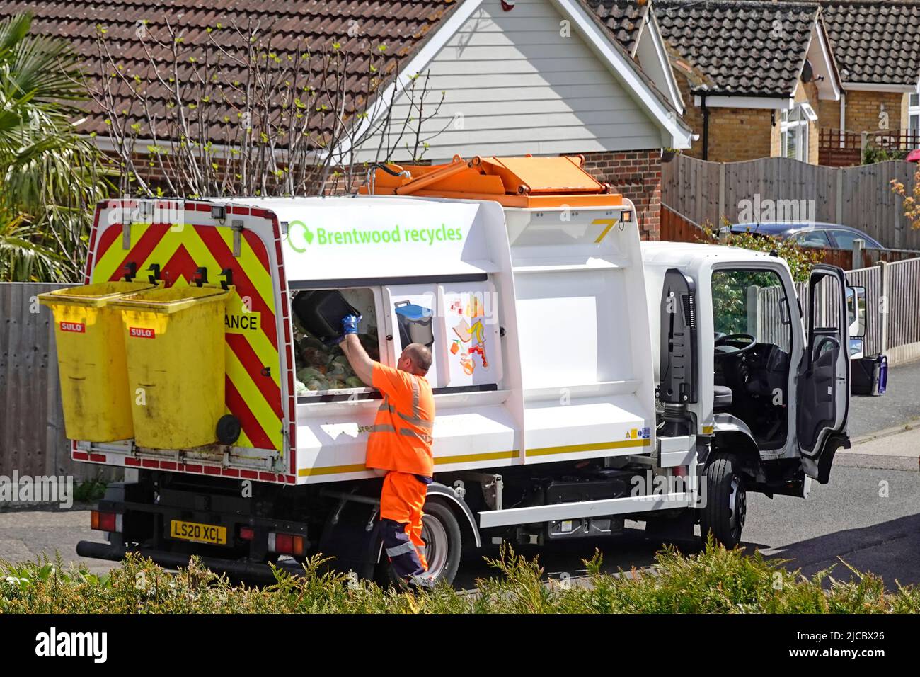 El conductor de camiones de reciclaje de contenedores de residuos de alta visibilidad vacía el carrito de casa en la parte trasera del camión de recogida especializado Brentwood Essex, Inglaterra, Reino Unido Foto de stock