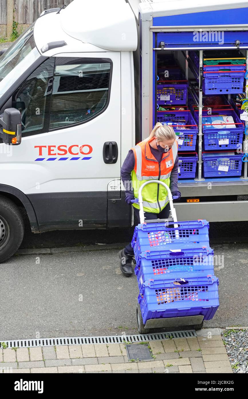 Supermercado Tesco entrega de compras en línea mujer camioneta conductor lleva uniforme de alta visibilidad personal empujando al cliente comida tranvía fuera de casa Inglaterra Reino Unido Foto de stock