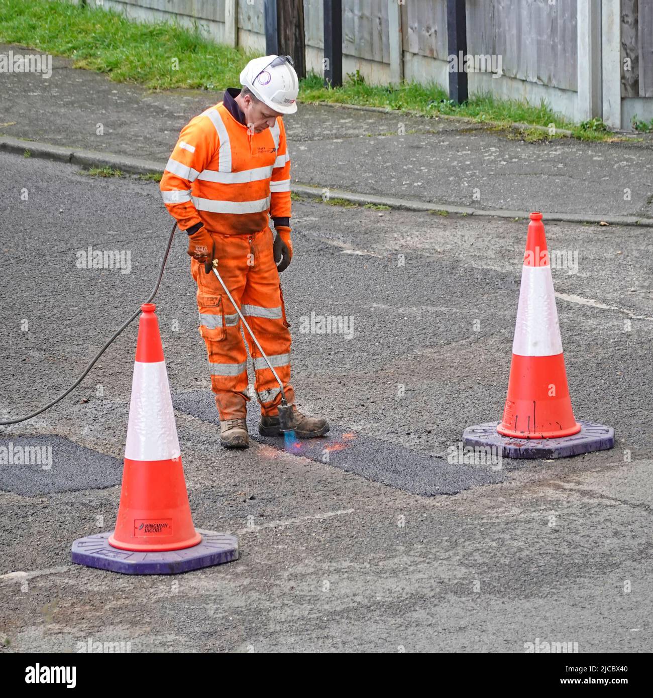Uno de los dos hombres equipo de alta visibilidad terminando la reparación de asfalto a pozos de pote en la carretera residencial mediante la calefacción de juntas con antorcha de gas propano Essex Inglaterra Reino Unido Foto de stock
