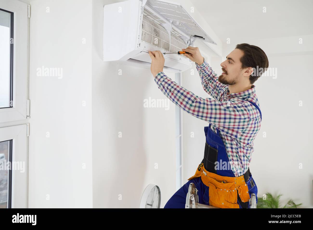 El mecánico masculino fija el acondicionador de aire en la casa del cliente Foto de stock