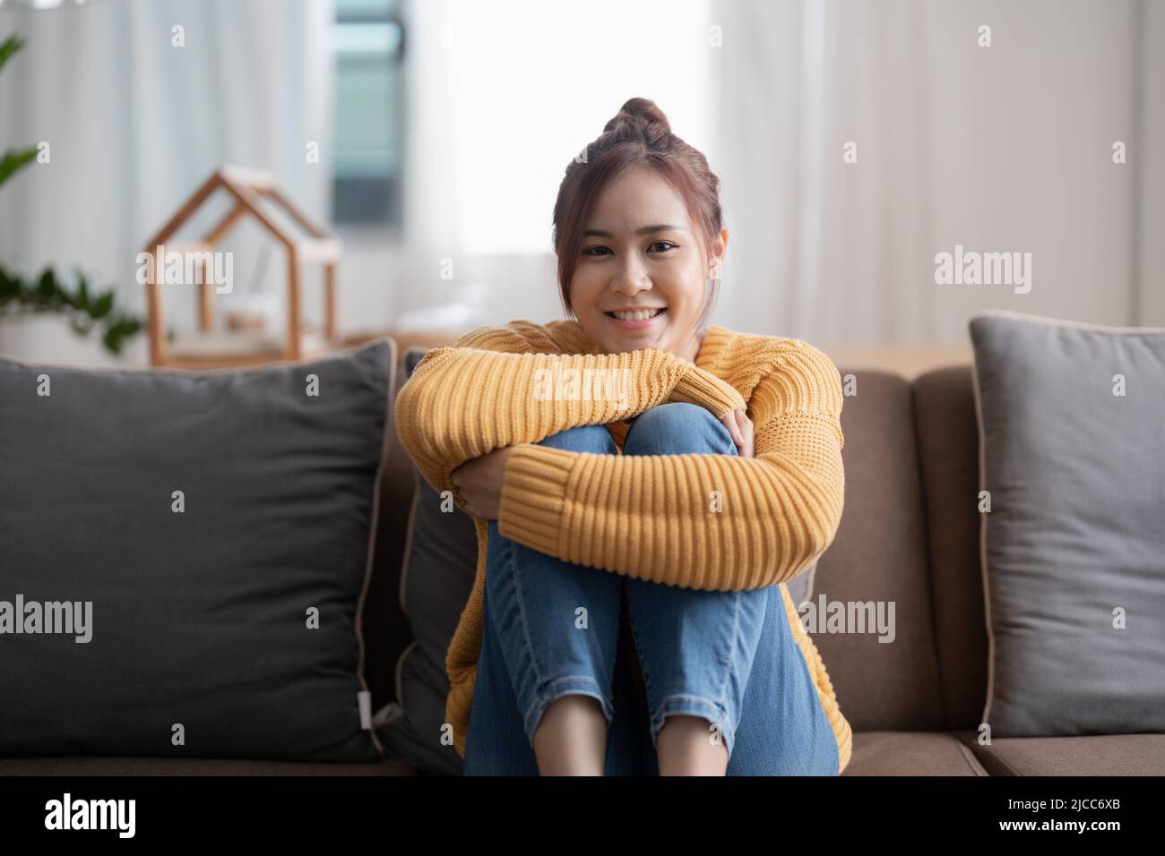 Mujer asiática tranquila relajándose en un cómodo sofá en la sala de estar, retrato mujer mirando en la cámara en un acogedor hogar Foto de stock