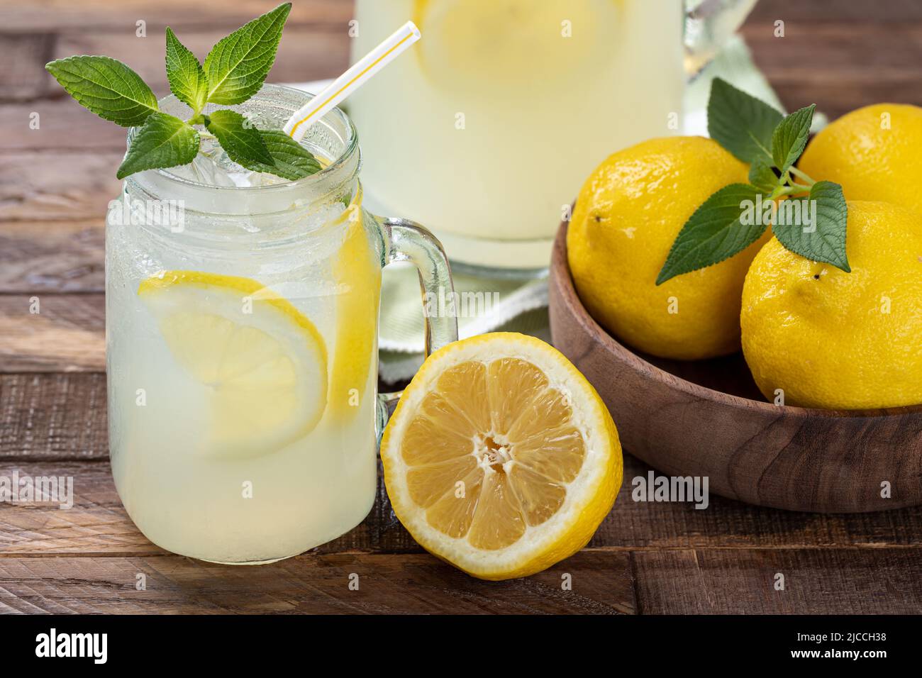Cierre de un vaso de limonada fría con menta, rodajas de limón y hielo sobre una mesa de madera Foto de stock