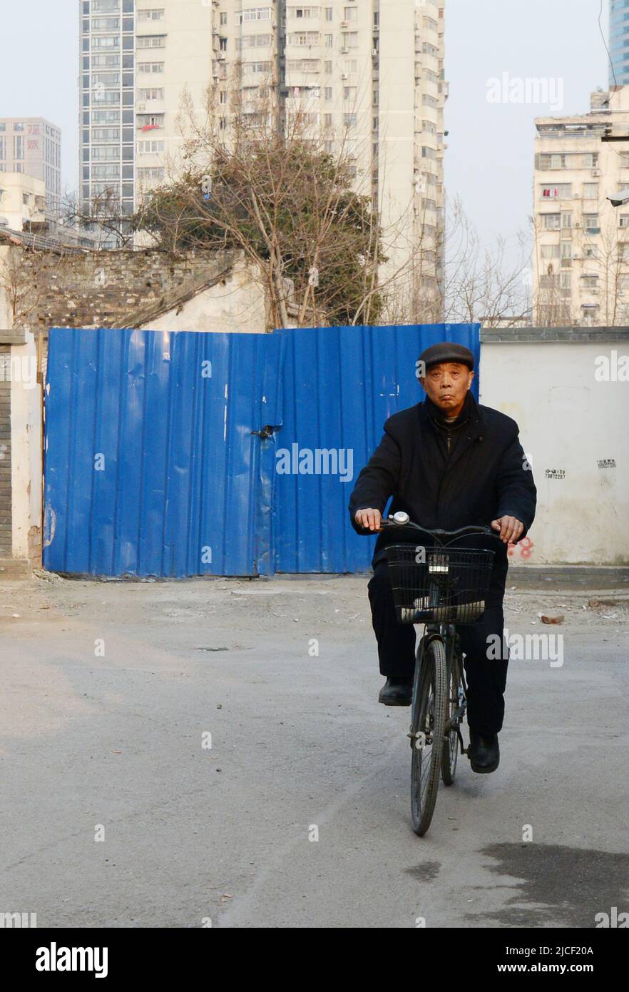 Un anciano chino montando su bicicleta en un área de hutong que será transformada en un moderno complejo de edificios en Nanjing, China. Foto de stock