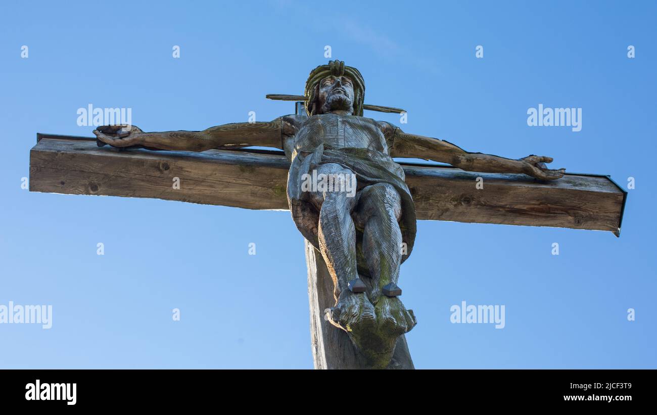 Oberammergau, Alemania - 31 de octubre de 2021: Jesucristo en la cruz. En la cima del Kofel (montaña). Fondo azul cielo. Foto de stock