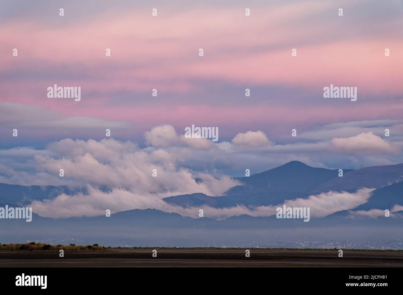 Las nubes se asientan en las colinas detrás de Nelson con el rosa temprano de la puesta de sol coloreando el cielo. Foto de stock