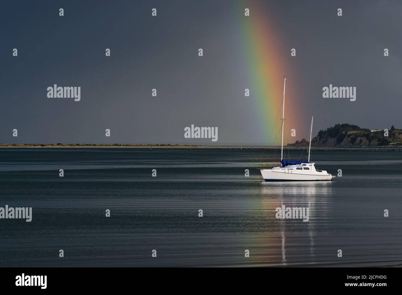 Un barco parece ser la olla de oro al final de un hermoso arco iris en un día tormentoso. Foto de stock