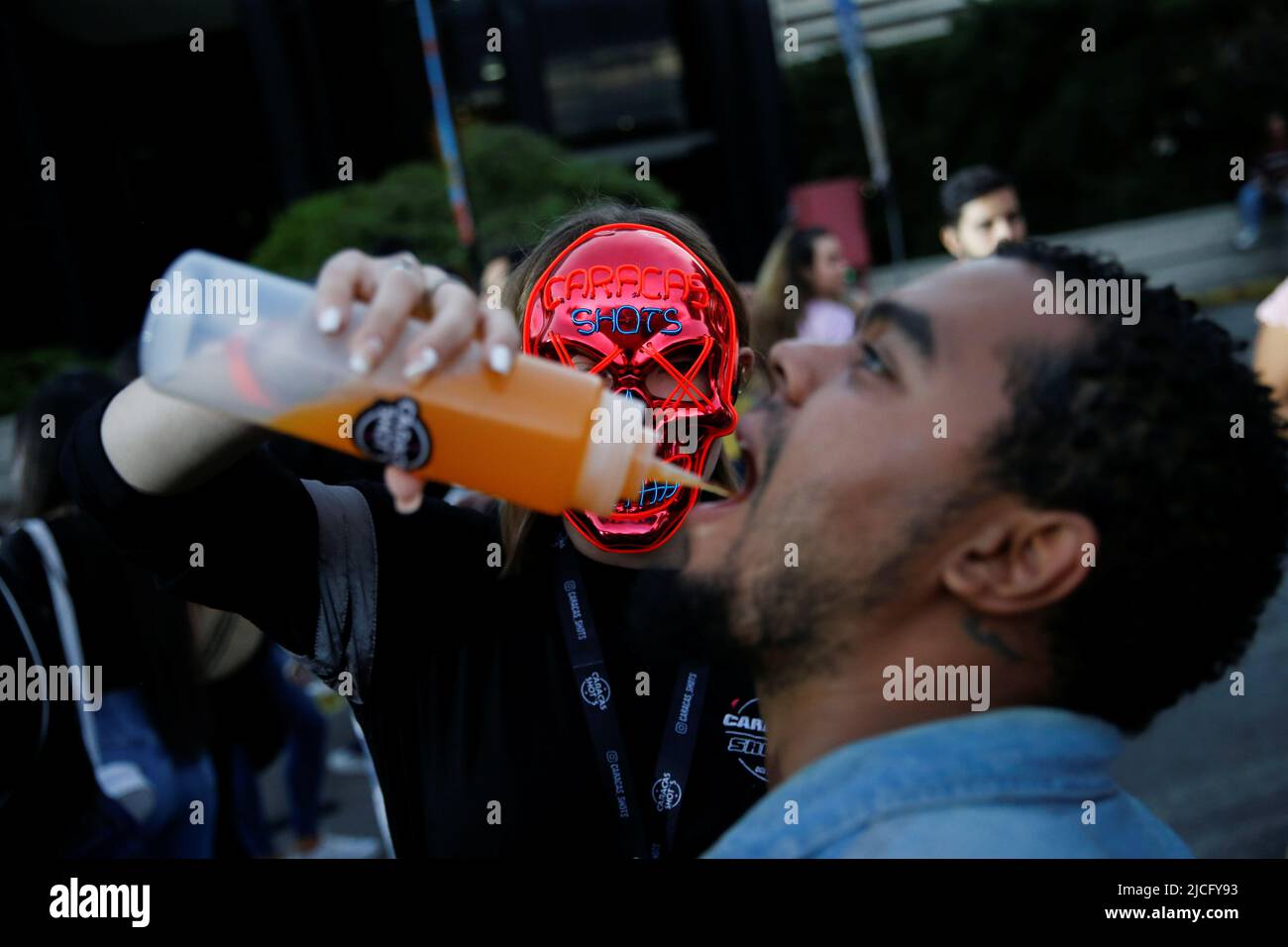 Una mujer que lleva una máscara de la película 'The Purge' le da a un  hombre una bebida durante un festival de música urbana albergado en el  estacionamiento abierto de un centro