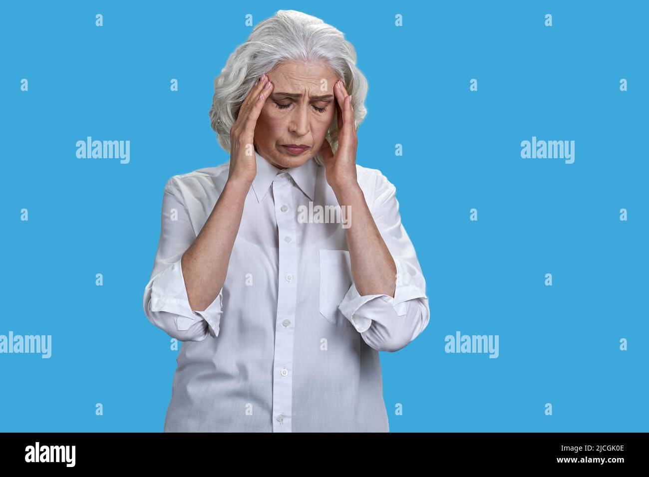 Mujer mayor con exceso de trabajo que sufre de dolor de cabeza contra fondo azul. Concepto de problema de salud. Foto de stock