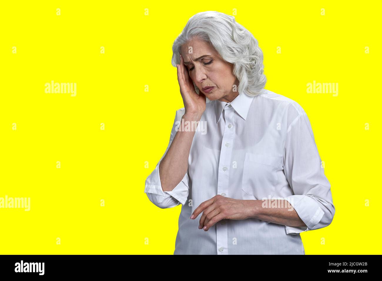 Mujer mayor estresada que sufre de migraña sobre fondo amarillo. Concepto de dolor de cabeza y problemas de salud. Foto de stock