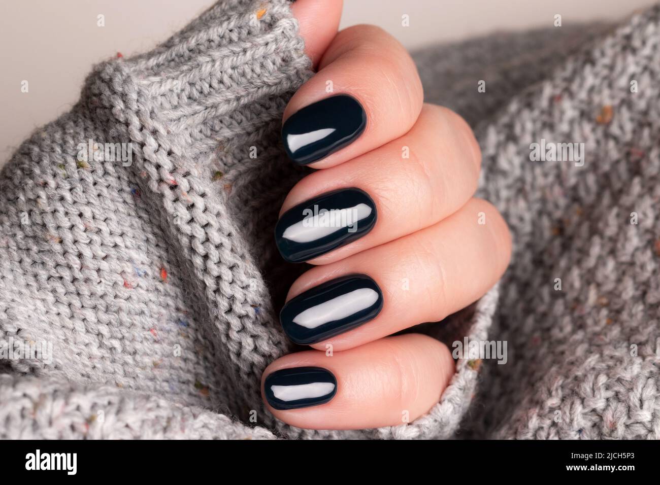 Mano femenina en jersey de punto gris con manicura hermosa - clavos negros  oscuros. Concepto de cuidado de uñas Fotografía de stock - Alamy