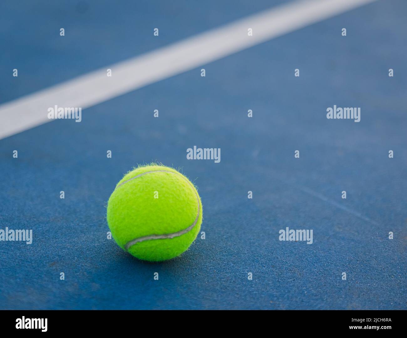 Primer plano de la pelota de tenis amarilla en una cancha dura azul. Foto de stock