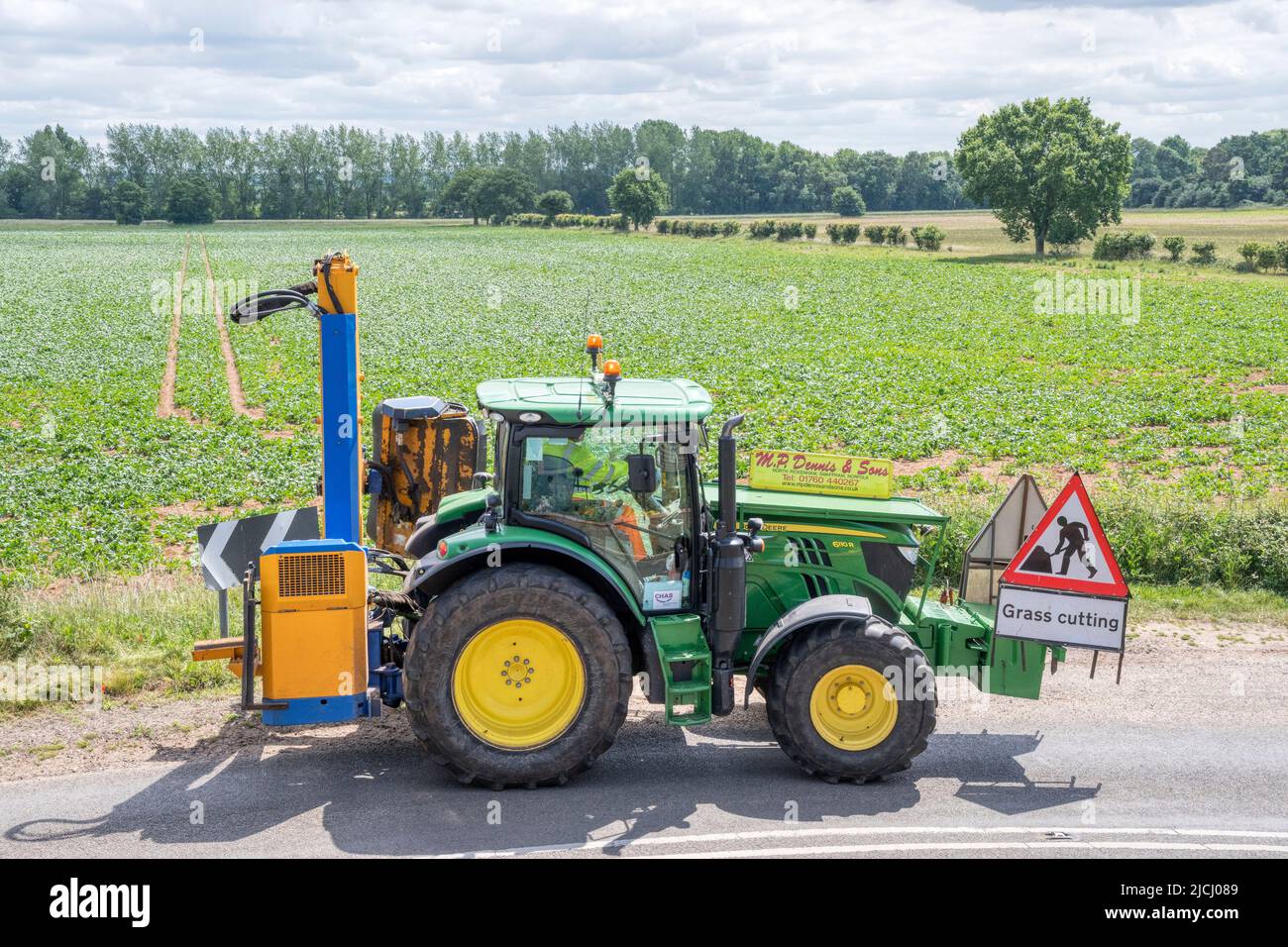 El contratista que usa el tractor John Deere 6110R para cortar hierba en verjas de carretera a lo largo de un carril de campo de Norfolk. Foto de stock