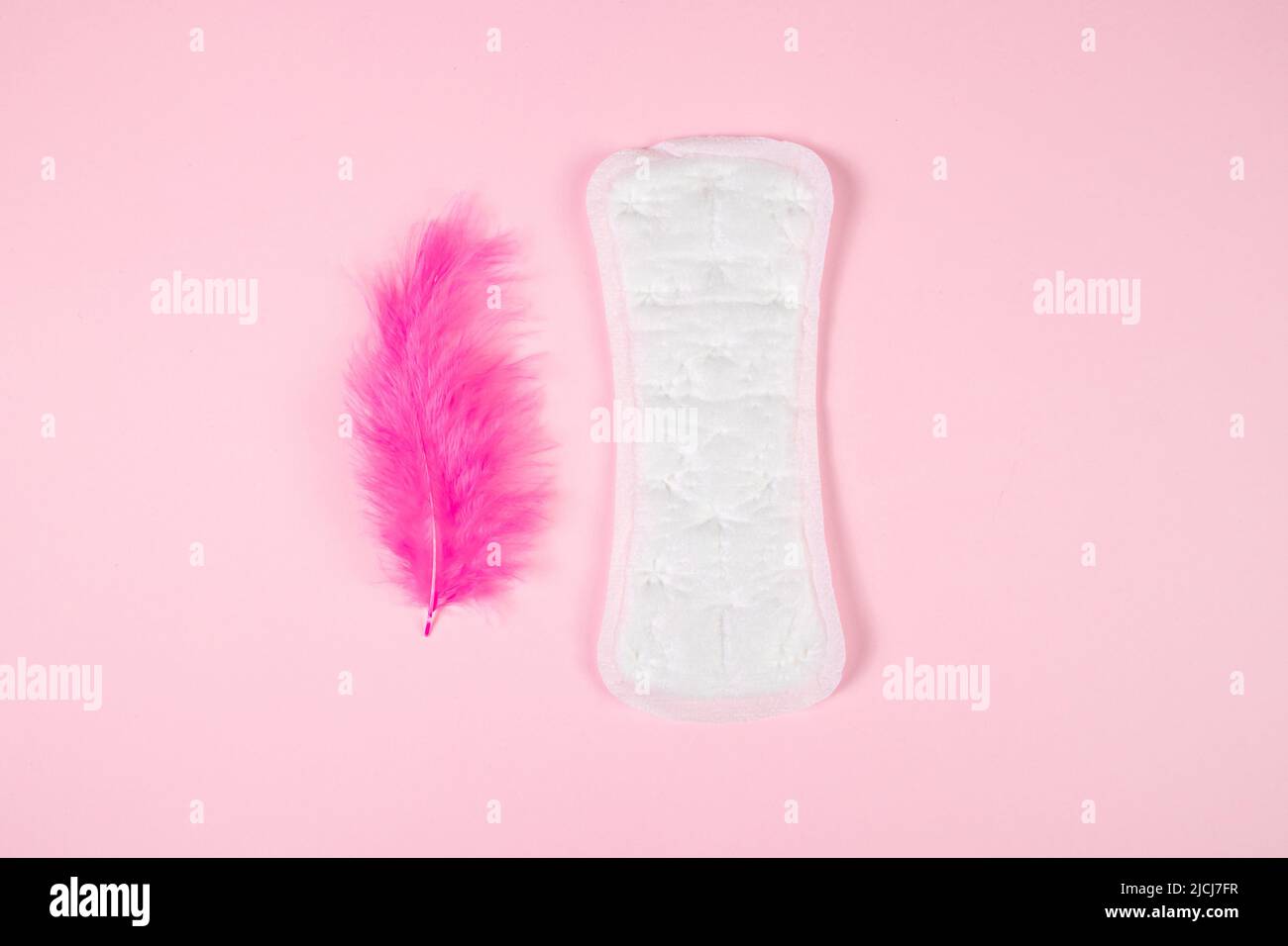 Almohadilla sanitaria y pluma rosa sobre fondo de color. Producto diario de higiene femenina. Menstruación y concepto de salud de la mujer. Foto de stock