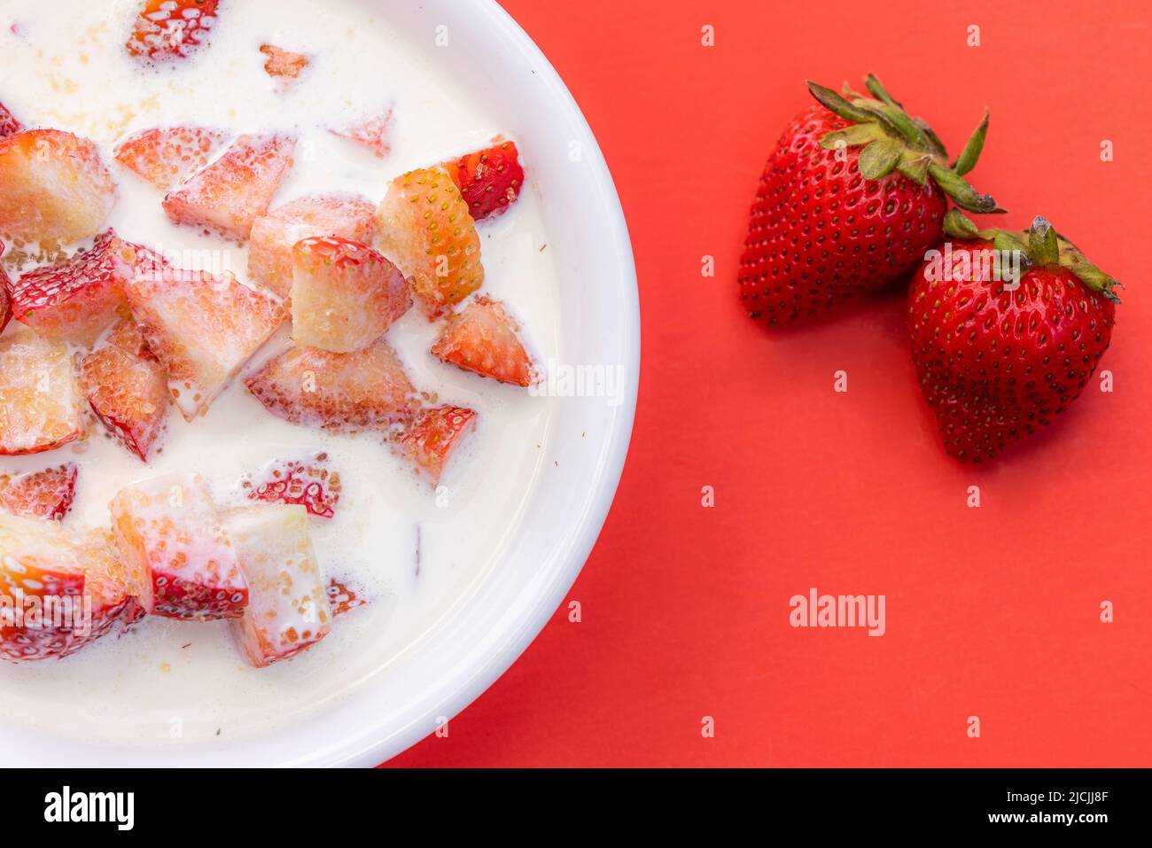 Fresas frescas con crema pesada y una espolvorea de azúcar sobre un fondo rojo Foto de stock