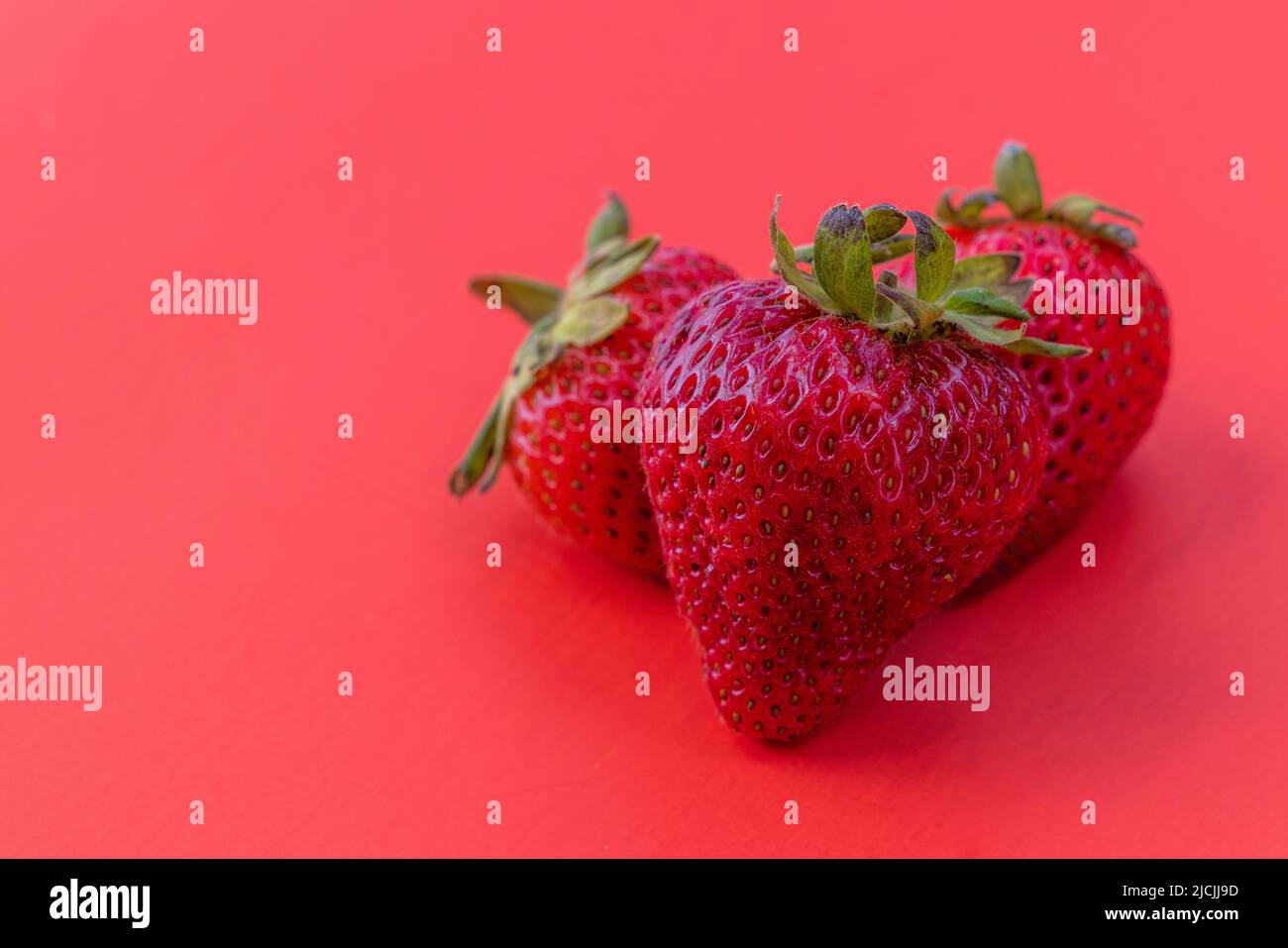 Primer plano de tres fresas frescas maduras sobre un fondo rojo Foto de stock