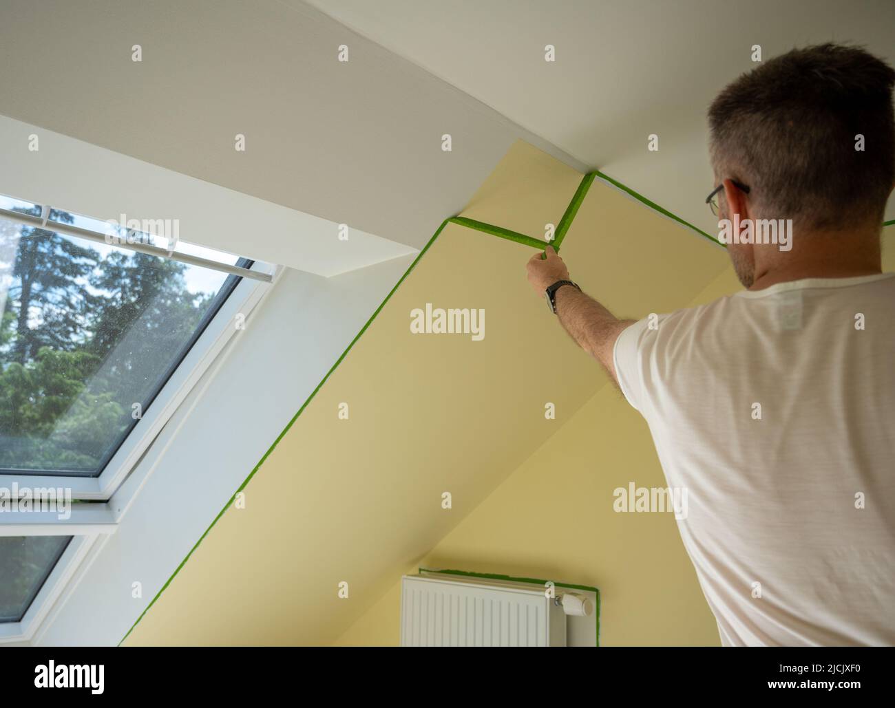 Painter elimina la cinta de enmascarar y crea un borde afilado entre una parte pintada de amarillo y blanco de una pared. Foto de stock