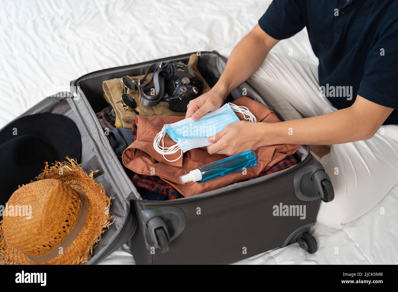 hombre mano equipaje de embalaje maleta con máscara facial y spray para proteger el coronavirus (covid-19) en una cama Fotografía de stock - Alamy