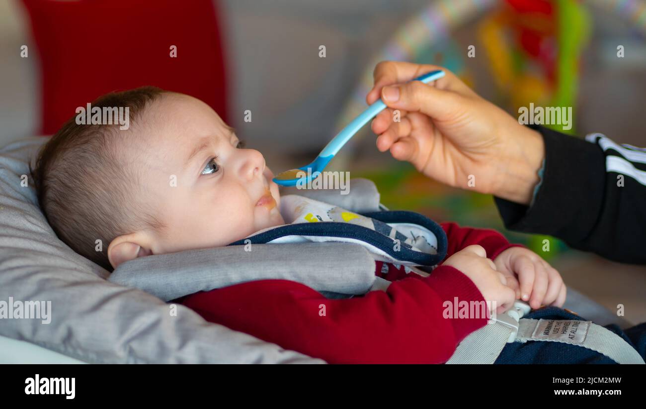 Primer plano de un bebé de unos meses de edad que comienza a destete comiendo un puré de frutas. Foto de stock