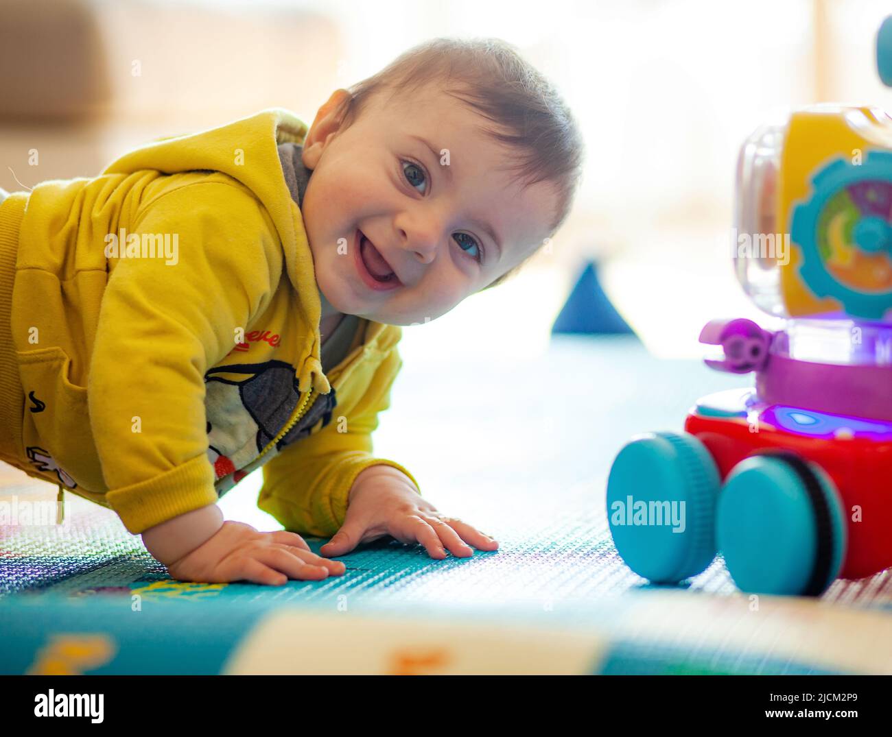 Un bebé de unos meses juega sonriendo en una alfombra suave junto con sus juguetes. Foto de stock